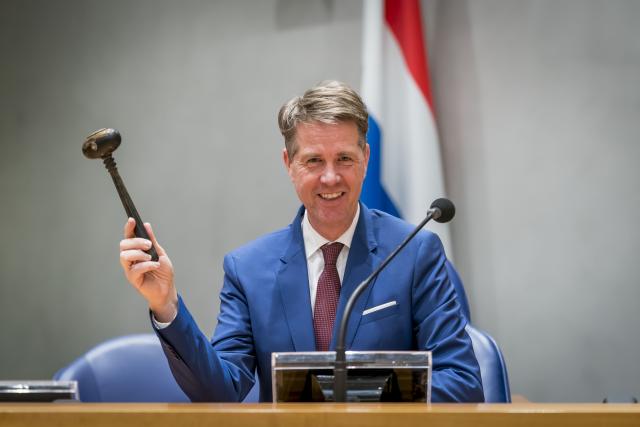 Chairman Martin Bosma is seated at the Chairman's seat in front of the Dutch flag. In his right hand he is holding the chairman's hammer.