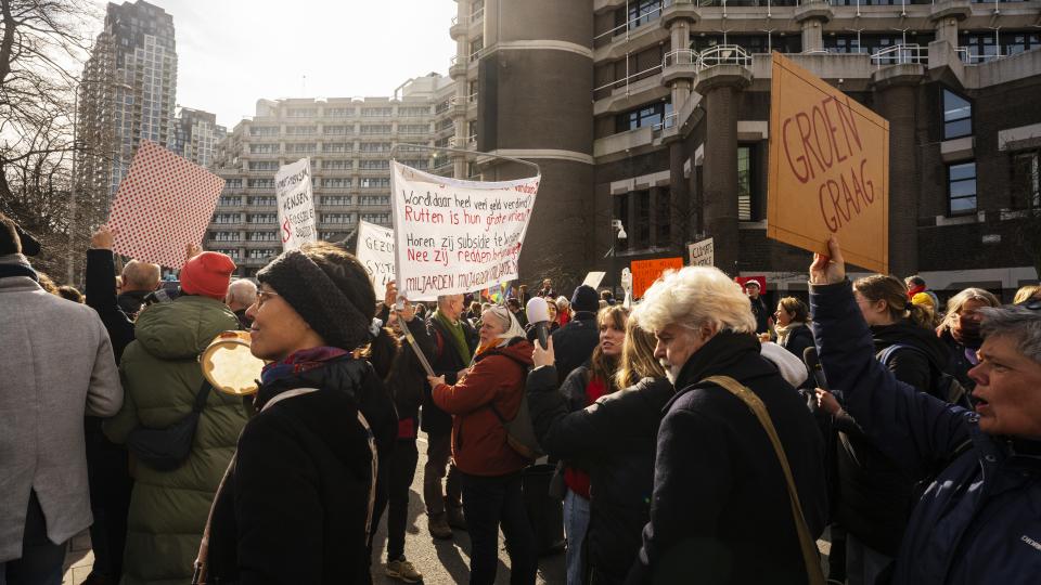 een groep mensen staat buiten de Tweede Kamer in protest met spandoeken.