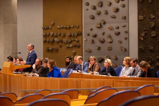 a minister is speaking into the microphone. Next to him people are sitting behind a panel