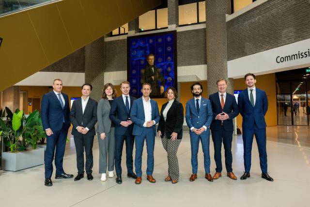 De leden van de commissie staand op een rij in de Statenpassage van de Tweede Kamer. 